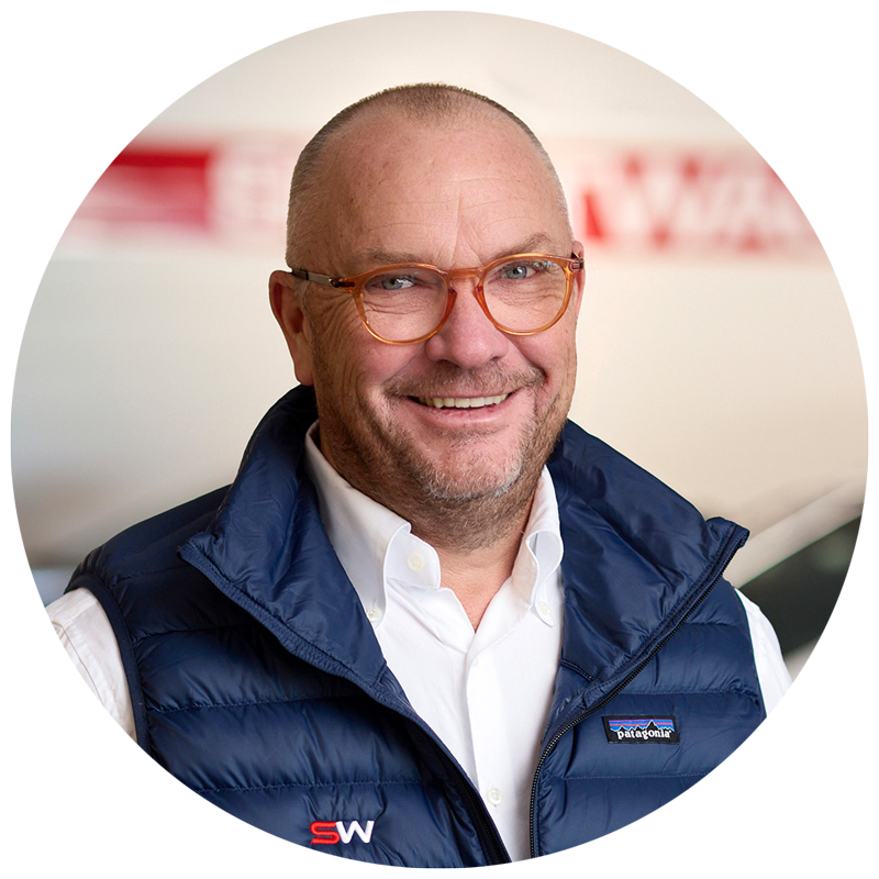 Smilende mann med briller og blå vest.